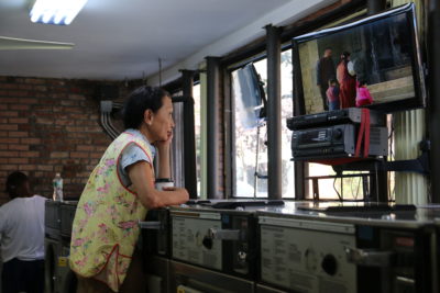 still from The Washing Society with woman watching TV at the laundromat