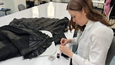Callie O'Connor sitting at a work table getting ready to stitch an old garment