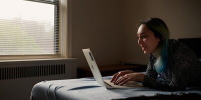 woman using her laptop on her bed near a window