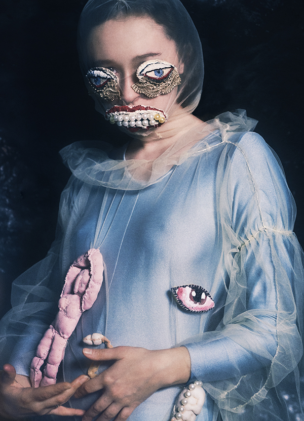 model wearing mask with exaggerated, illustrated eyes and mouth and a dress with an illustrated eye, holding a doll