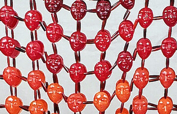 closeup of a beaded shirt where the 'beads' are heads of varying shades of red