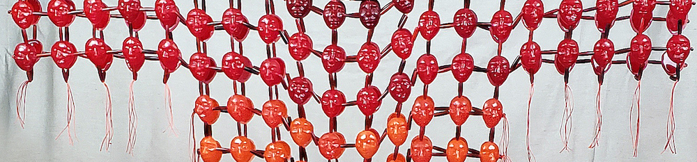 closeup of a beaded shirt where the 'beads' are heads of varying shades of red