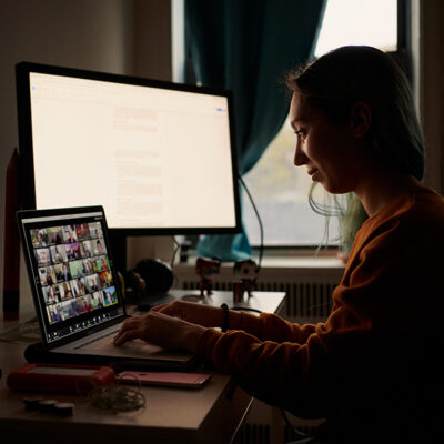 woman sitting at a laptop computer with a larger desktop monitor behind it